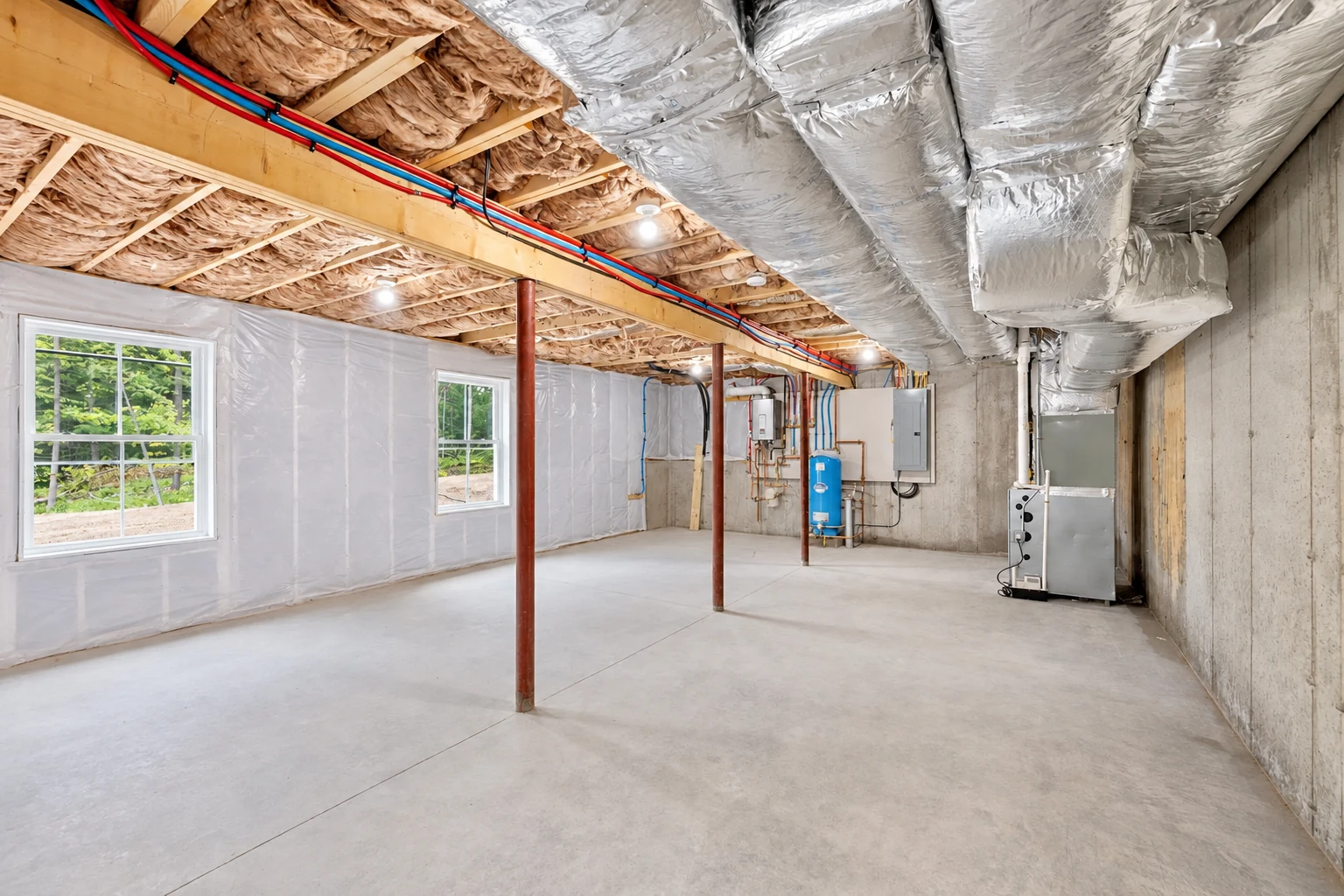 Unfinished basement with fiberglass insulation between ceiling joists, large silver HVAC ducts, and a concrete floor.