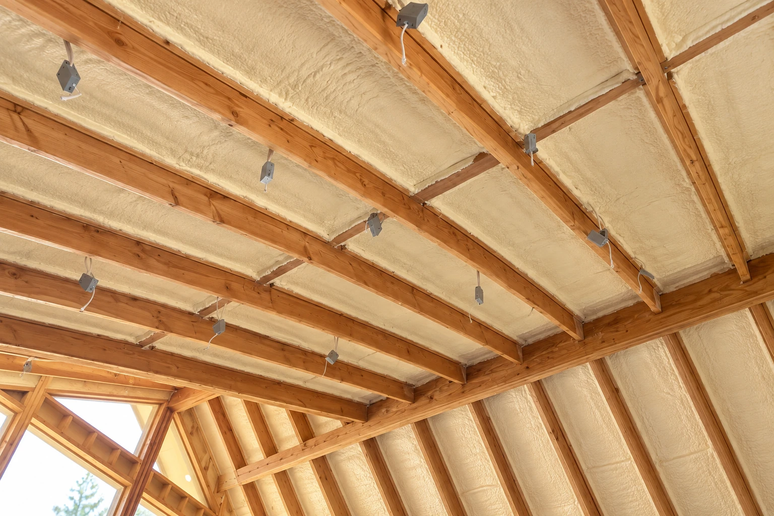 Open-cell spray foam fills the roof and wall cavities of a timber-framed room, with exposed rafters and wiring visible.