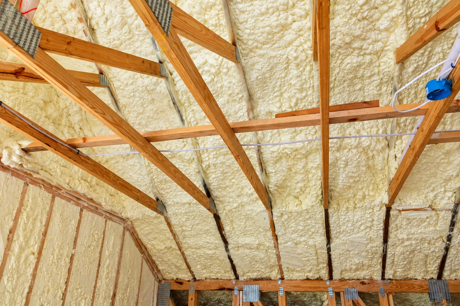 Yellow spray foam fills the roof and wall cavities between exposed wooden rafters and studs.